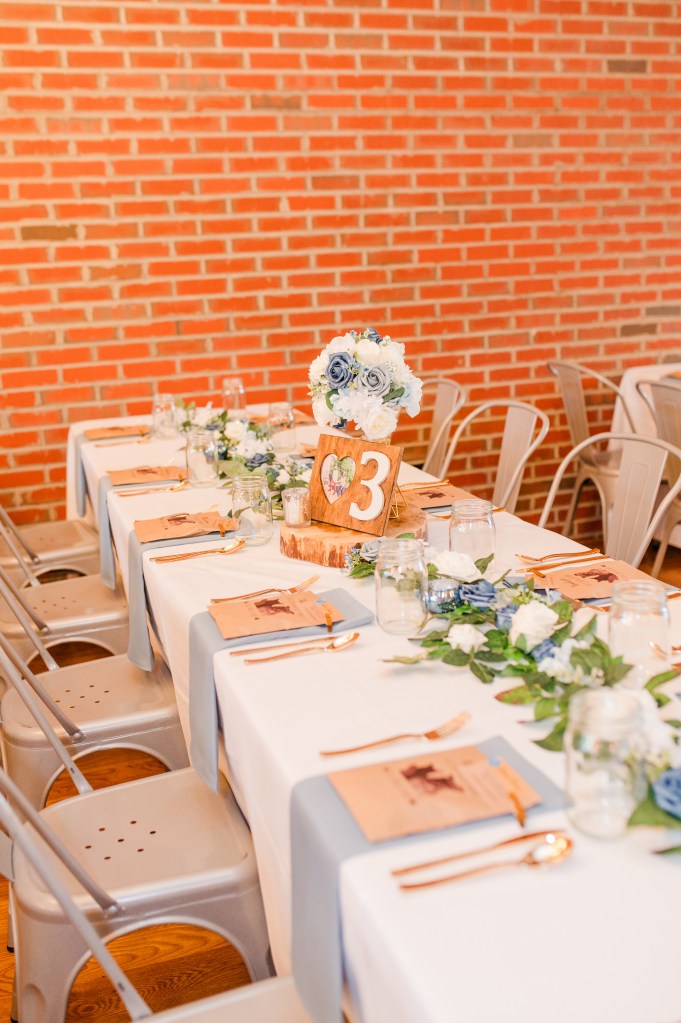A long banquet table covered in a white tablecloth with place settings and a floral runner.